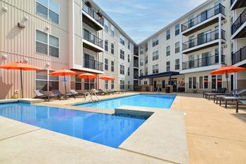 A swimming pool surrounded by apartment buildings and lounge chairs.